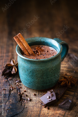 Cup of hotchocolate with a cinnamon stick, star anise and grated dark chocolate as a topping on dark rustic wooden background