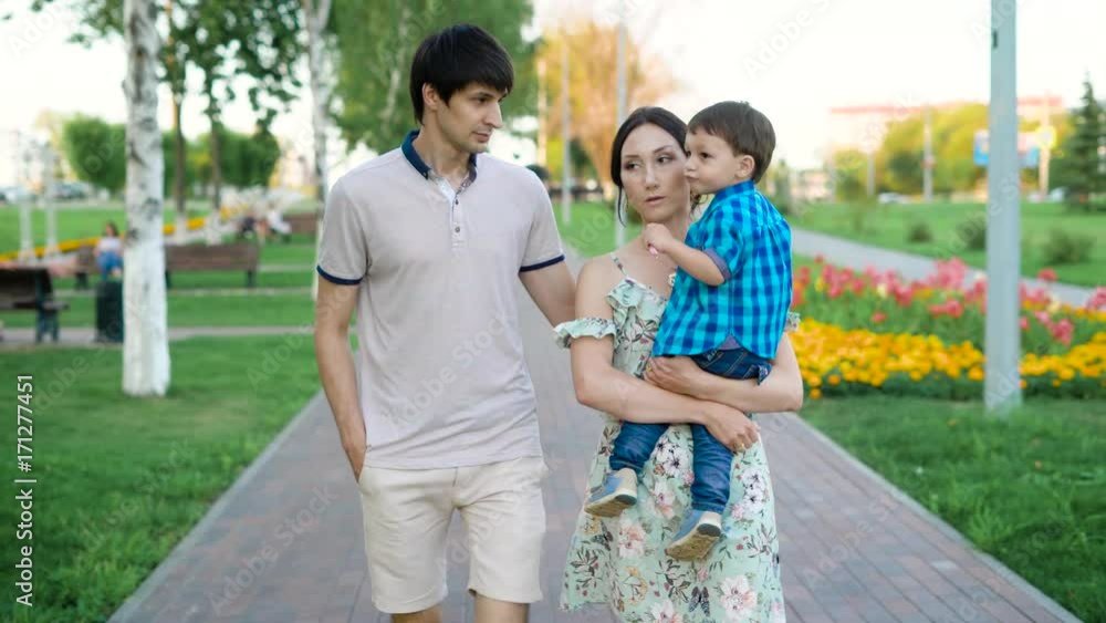 happy young family is strolling in a park in summertime, mother is holding her little son on hands happy young family is strolling in a park in summertime, mother is holding her little son on hands