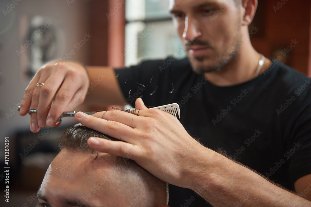 Selective focus on the hands of a professional barber giving his client a haircut. 
