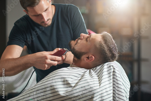 Horizontal shot of a professional barber working at his barbershop trimming beard of a young man copyspace. 