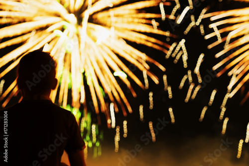 Unrecognizable silhouette of a boy with his back to us, who watches the show Fireworks. Festive background with place for text