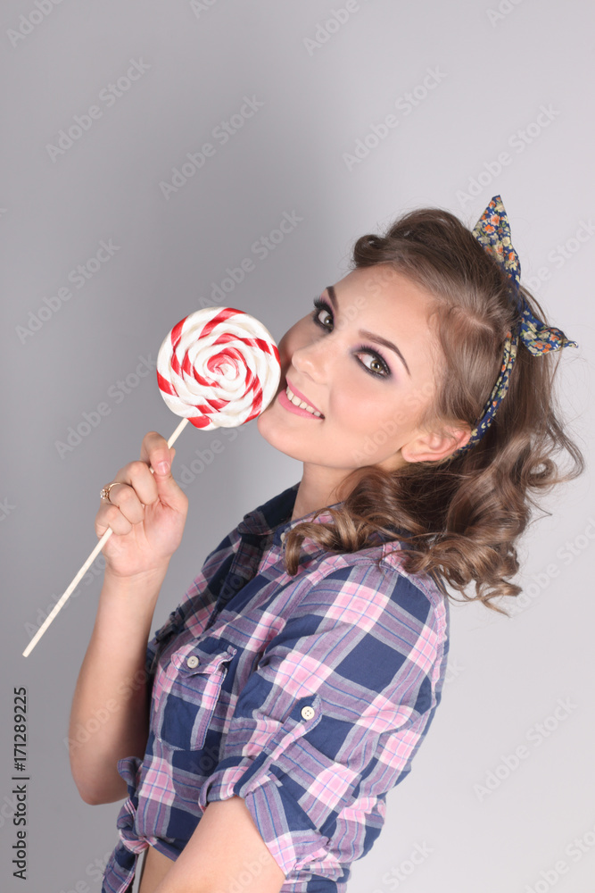 Pinup beautiful girl in checkered shirt poses with lollipop in studio