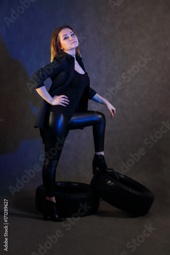 Women with make-up in black poses on tires in studio with blue light