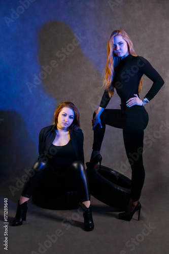Two young women with make-up in black poses in studio with blue light