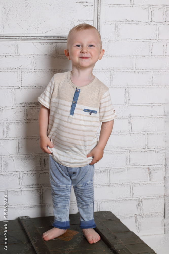 Happy handsome little boy smiles and stands on wooden box in room Happy handsome little boy smiles and stands on wooden box in room