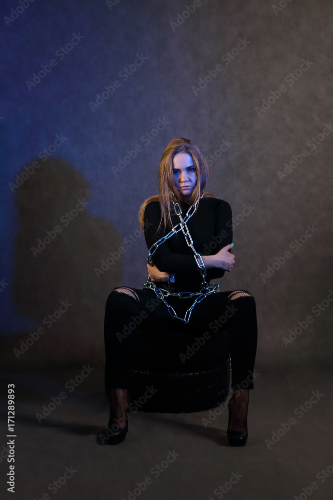 Women in black clothes in chain poses on tires in studio with blue light