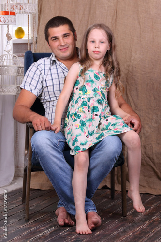 Happy father in shirt and barefoot daughter sit together in armchair in studio © singulyarra