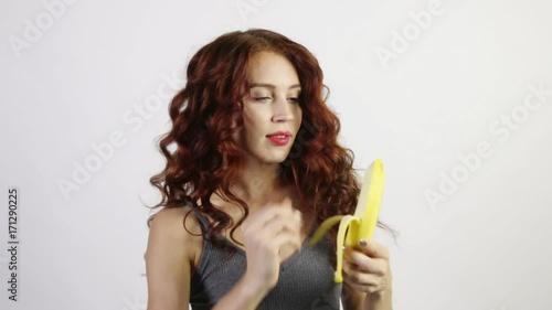 Pretty young woman peels and eats banana in white studio, video with sound