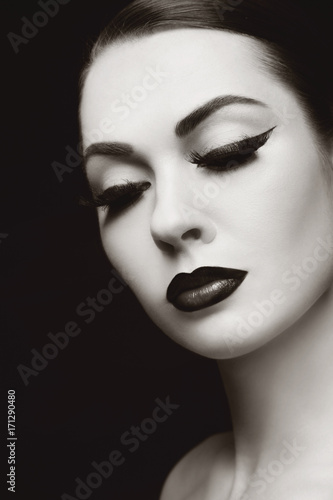 Vintage style duotone portrait of young beautiful woman with winged eye make-up, copy space