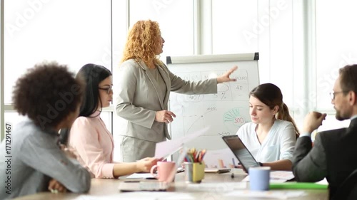 Mid aged foxy businesswoman making presentation for clients. Negotiations in the office, female standing by the chart.