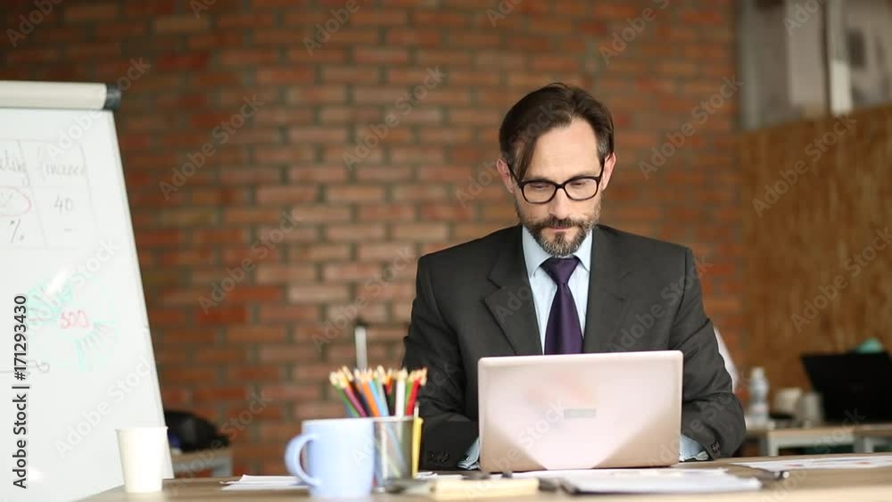 Close up view of angry businessman sitting in his office. Man in busines suit sitting at table, looking in laptop. Close up view of angry businessman sitting in his office. Man in busines suit sitting at table, looking in laptop.