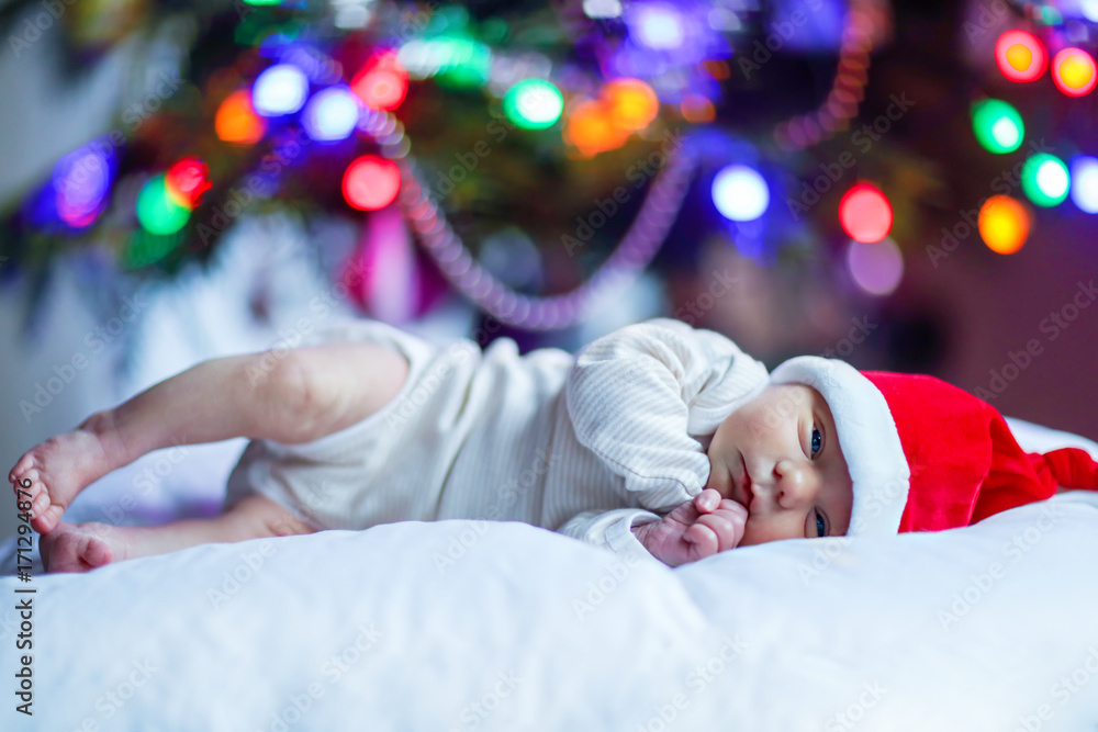 One week old newborn baby in Santa hat near Christmas tree One week old newborn baby in Santa hat near Christmas tree