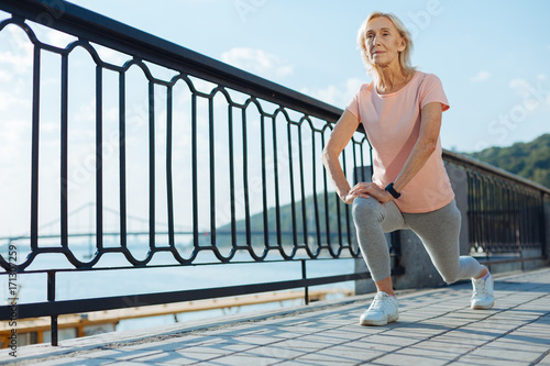Slender elderly woman doing lunges on the bridge