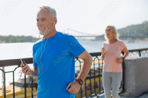 Joyful senior man listening to music while jogging with wife