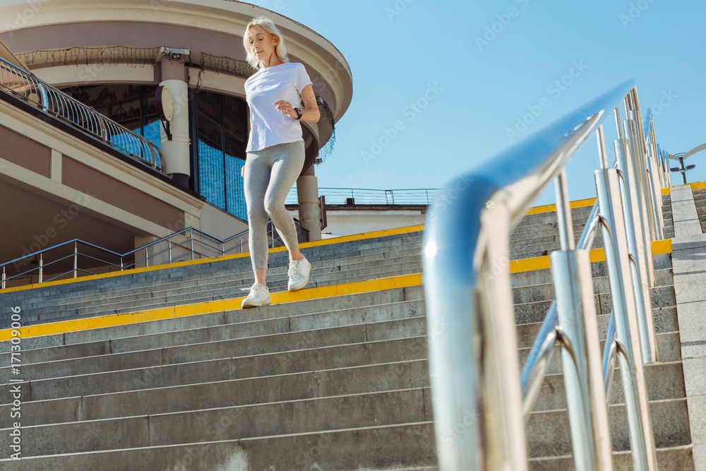Naklejka premium Slim senior woman in sporty outfit running down the stairs