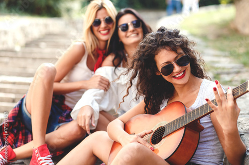 Group of young female friends sitting on the stairs singing and playing guitar. © Zoran Zeremski