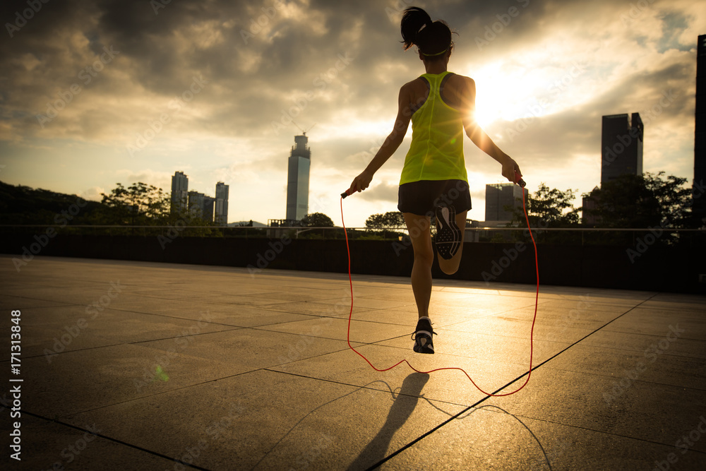 Young fitness woman jumping rope at sunrise city building roof