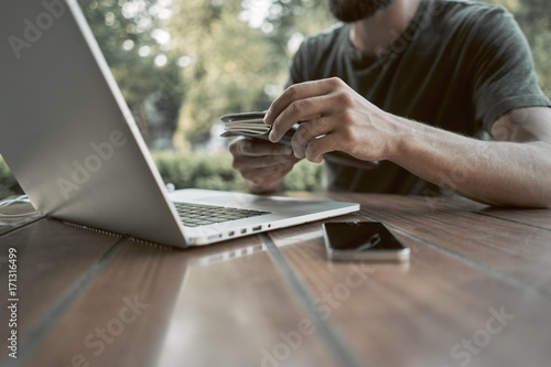 Close-up. A young man is sitting in front of a laptop. Blurred background of the park