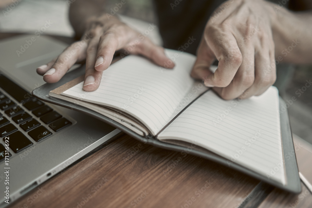 Close-up. The young man opened a notebook on the table. there is a laptop near by Close-up. The young man opened a notebook on the table. there is a laptop near by