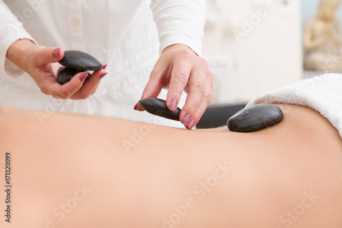 Schilderij op canvas Im Massagesalon werden heisse Steine auf den Rücken einer Frau gelegt