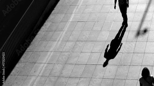 City people walking at sunset. Silhouettes and shadows on the pavement of the street. Urban scene, city life and job concept. Black and white