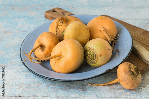  Vegetables.  Fresh raw turnip in a blue round bowl, next to a cutting board and a knife on an old wooden table.