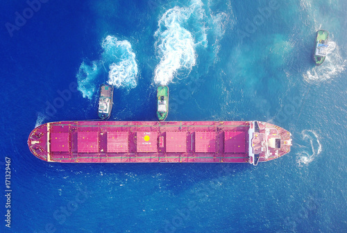 Large bulk carrier ship pulled by tow-three  tugboats in the port 