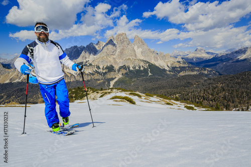 Mountaineer backcountry ski spring walking up along a snowy ridge with skis in the backpack. In background blue cloudy sky and shiny sun and Monte Cristallo in South Tirol, Dolomites, Italy. 
