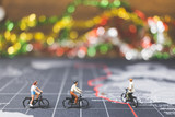 Miniature people travelers riding bicycle on world map