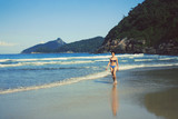 mid age woman in swimsuit walking along the seashore, Brazil