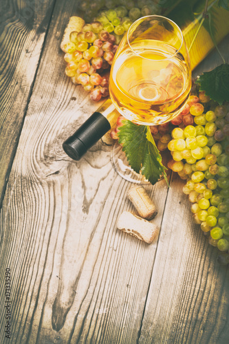 Бутылка белого вина, винограда и пробки на деревянном столе