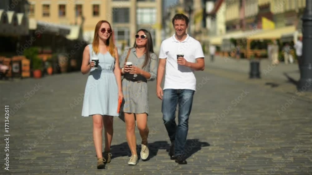 Three Happy Friends Drinking Coffee while Walking around the City. Full Height Portrait of Two Girls and One Boy with Beverages in the Hands. Three Happy Friends Drinking Coffee while Walking around the City. Full Height Portrait of Two Girls and One Boy with Beverages in the Hands.