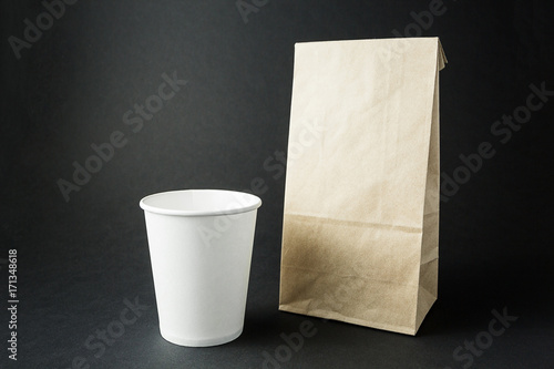 White paper cups and a packing bag from recycled paper layout on a black background, space for text or labels.
