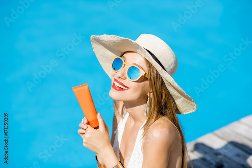 Φωτογραφία Portrait of a young woman in sunhat and swimsuit holding a tube with sunscreen l