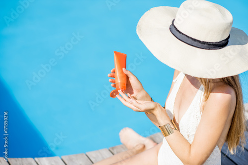 Young beautiful woman applying sunscreen lotion sitting on the wooden poolside. Sunscreen solar cream uv protection concept © rh2010