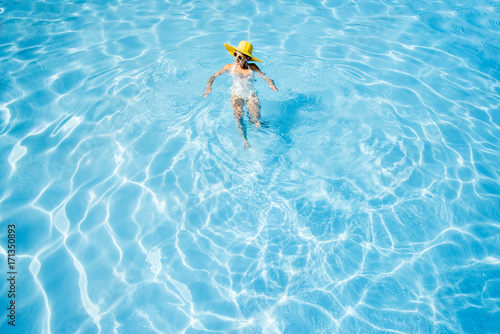 Young woman in yellow sunhat swimming at the basin with blue water. General view from above