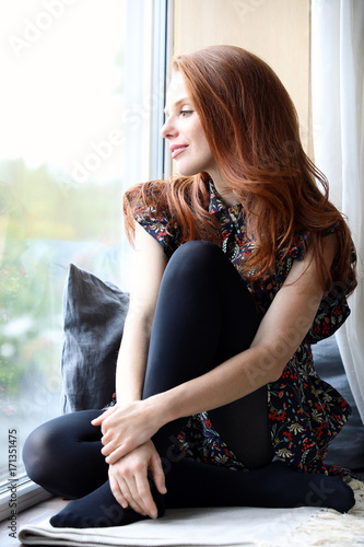 Foto Hübsche rothaarige Frau sitzt am Fenster