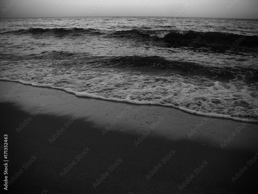 Waves and the sea shore in the evening. Monochrome photo.