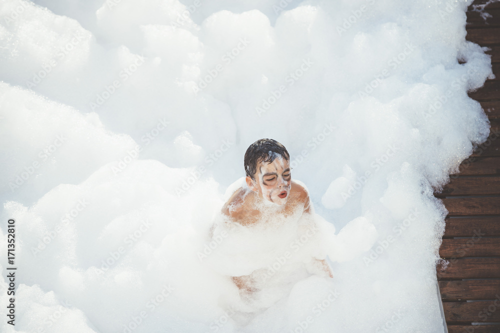 Cheerful kid playing in white foam Cheerful kid playing in white foam