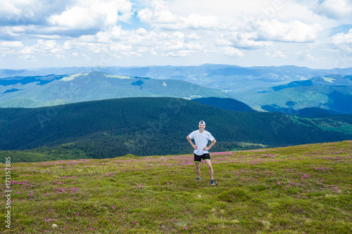 Young man Hiking at Carpathians Mountains stands on top of a hill, against a backdrop of beautiful mountains and a blue sky
