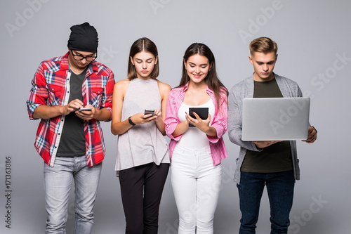 Beautiful young people of different nationalities are using gadgets and smiling, standing against white brick wall photo