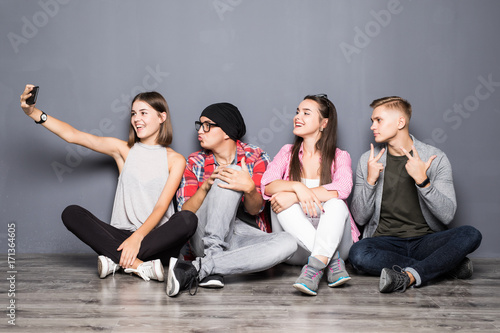 Happy friends taking selfie while sitting on floor