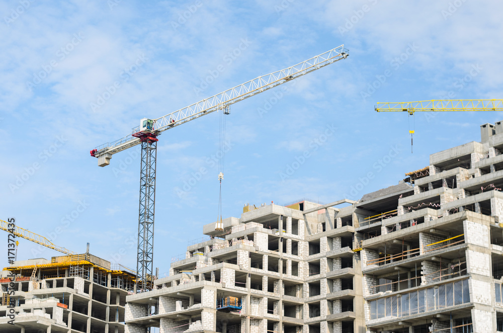 Construction site. Construction cranes and high-rise building under construction against blue sky.