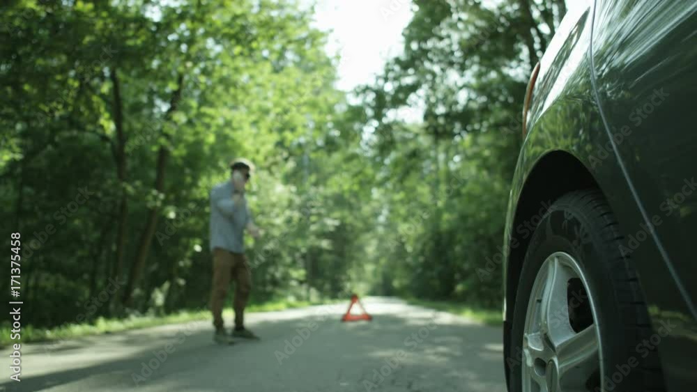 Car's Rear Wheel. Young Man Talking on the Phone Car's Rear Wheel. Young Man Talking on the Phone
