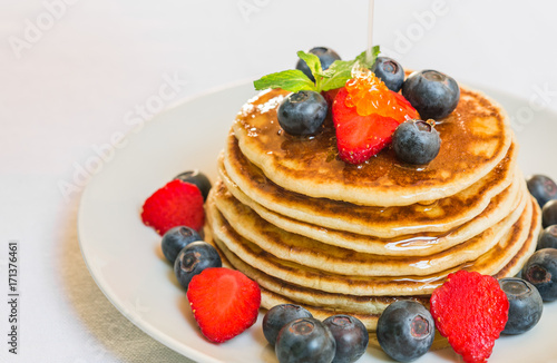 American pancakes with blueberries, strawberries, and honey against white background