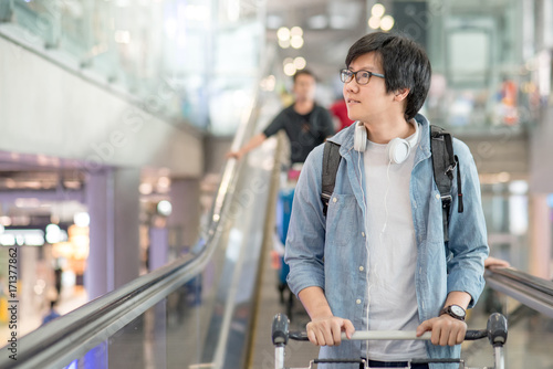 Young Asian man with airport trolley on escalator  walking to check-in counter in the international airport terminal. travel abroad on vacation