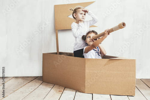 Two children little girls home in a cardboard ship play captains and sailors