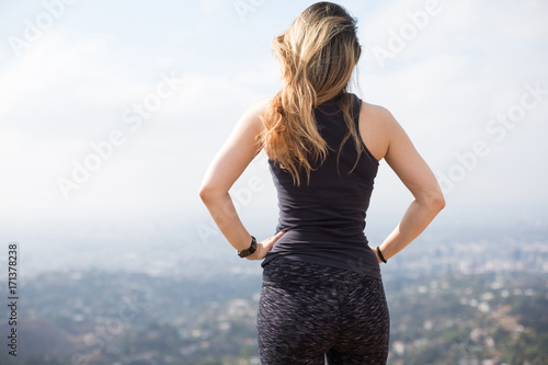 Fototapeta A confident young girl standing on the top of the hill with her hands on her  wa