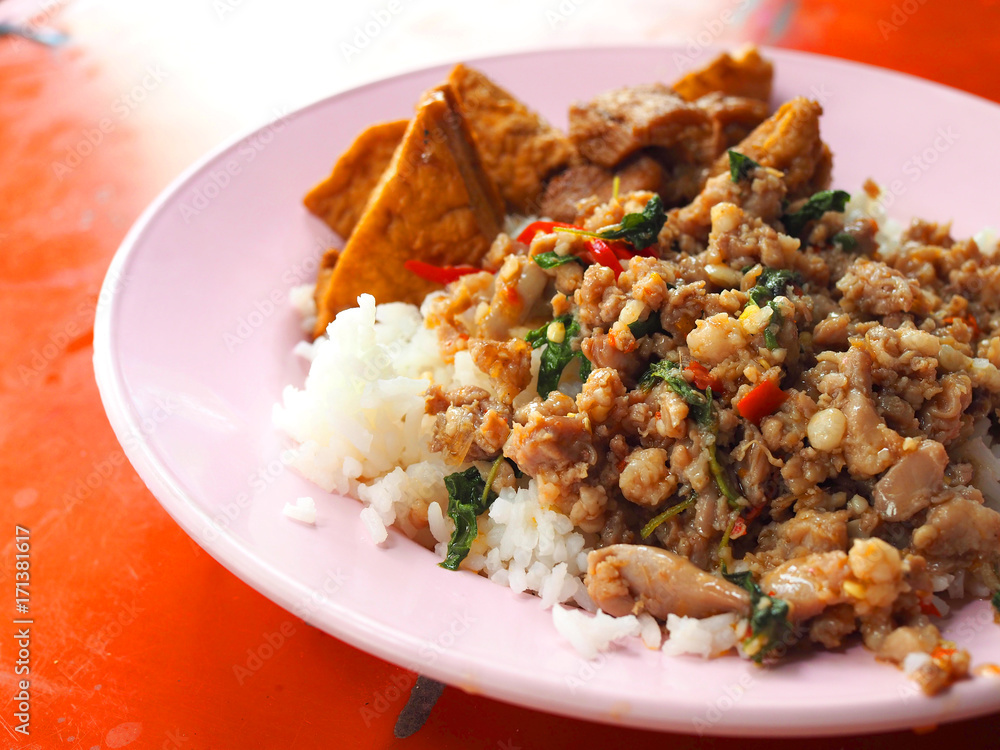 Close up perspective of Thai local traditional street food stall: stir fried spicy minced pork with holy basil, big chunk of deep fried tofu boiled in black sweet brown Chinese sauce, topped on rice Close up perspective of Thai local traditional street food stall: stir fried spicy minced pork with holy basil, big chunk of deep fried tofu boiled in black sweet brown Chinese sauce, topped on rice