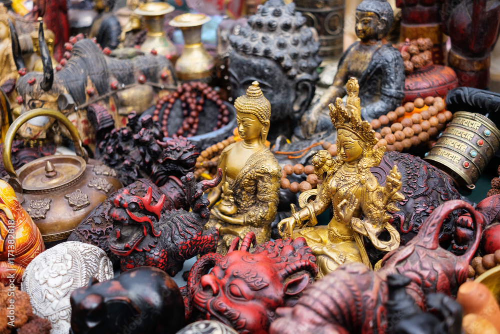 Nepalese religious statuettes made of brass surrounded by other handicrafts and souvenirs on the market, Kathmandu, Nepal. Text on the praying wheels - mantra Om Mani Padme Hum written in Sanskrit. Nepalese religious statuettes made of brass surrounded by other handicrafts and souvenirs on the market, Kathmandu, Nepal. Text on the praying wheels - mantra Om Mani Padme Hum written in Sanskrit.